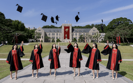 Graduates in academic gowns toss their graduation caps in the air on a university campus.